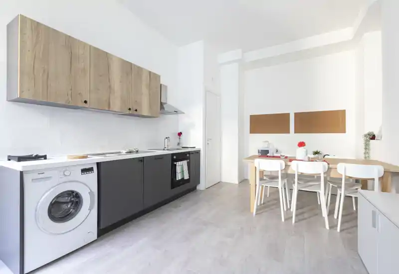 Cuisine moderne et lumineuse avec appareils intégrés et une petite table pour quatre personnes ; meubles en bois clair et sol pâle apportent une atmosphère aérée.