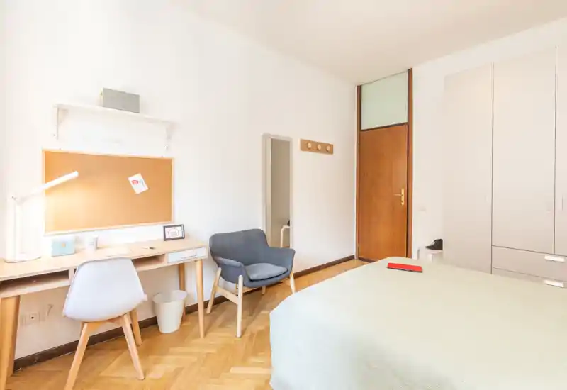 Camera luminosa e ordinata con letto matrimoniale, comodino e una piccola scrivania. Presenza di una poltrona comoda, armadio a muro e pavimento in parquet che rendono l'ambiente accogliente.