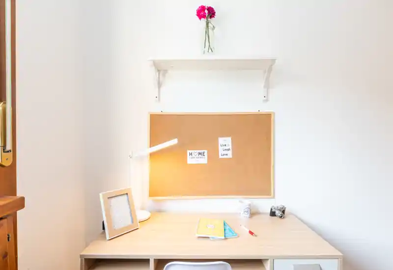 Spazio di lavoro domestico luminoso e minimale con scrivania in legno, bacheca, lampada e decorazioni semplici — perfetto per studiare o lavorare.