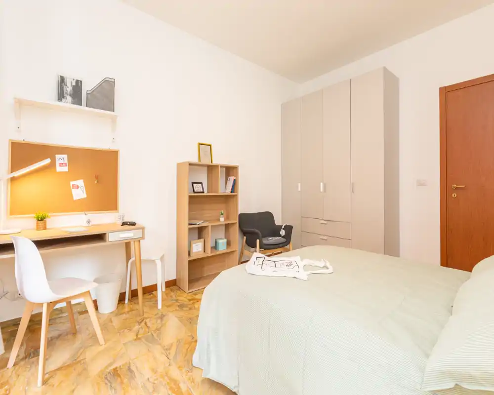 Dormitorio luminoso y bien decorado con cama visible, zona de escritorio y armario. Tonos cálidos y orden generan un ambiente acogedor y funcional, ideal para un anuncio de alquiler.