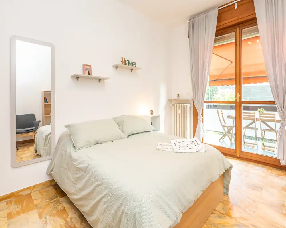 Dormitorio luminoso y bien decorado con cama doble, ropa de cama acogedora y acceso directo a un balcón que aporta mucha luz natural.