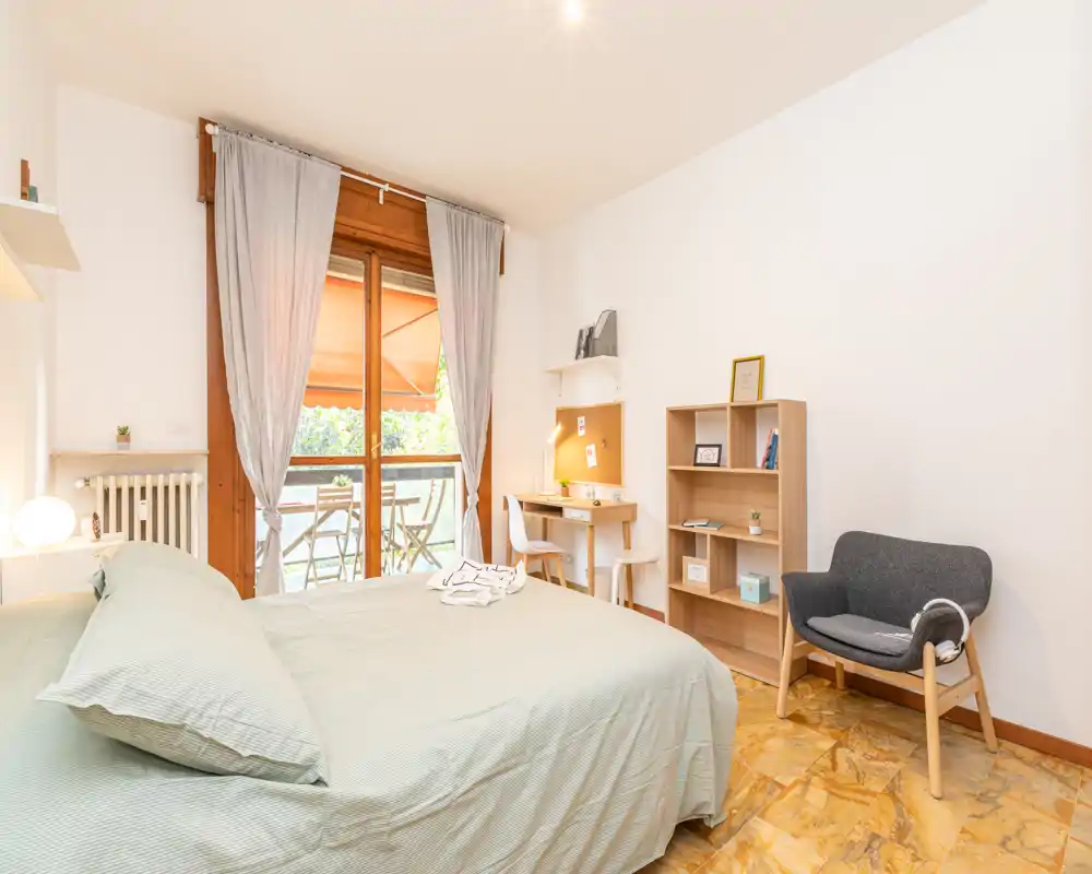 Dormitorio luminoso y bien decorado con cama grande, zona de escritorio y acceso al balcón. Ropa de cama verde suave y detalles en madera ofrecen un ambiente tranquilo y acogedor.