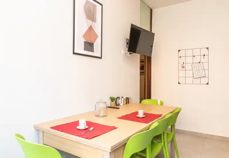 Zona pranzo luminosa e moderna con tavolo in legno chiaro, sedie verdi vivaci e decorazioni semplici per un ambiente accogliente e fresco.