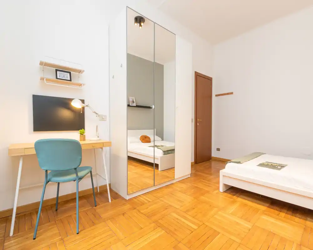 Camera da letto luminosa e moderna con letto singolo, armadio con ante a specchio e scrivania. Pavimento in parquet pulito, arredamento minimale e illuminazione gradevole, perfetta per un annuncio.