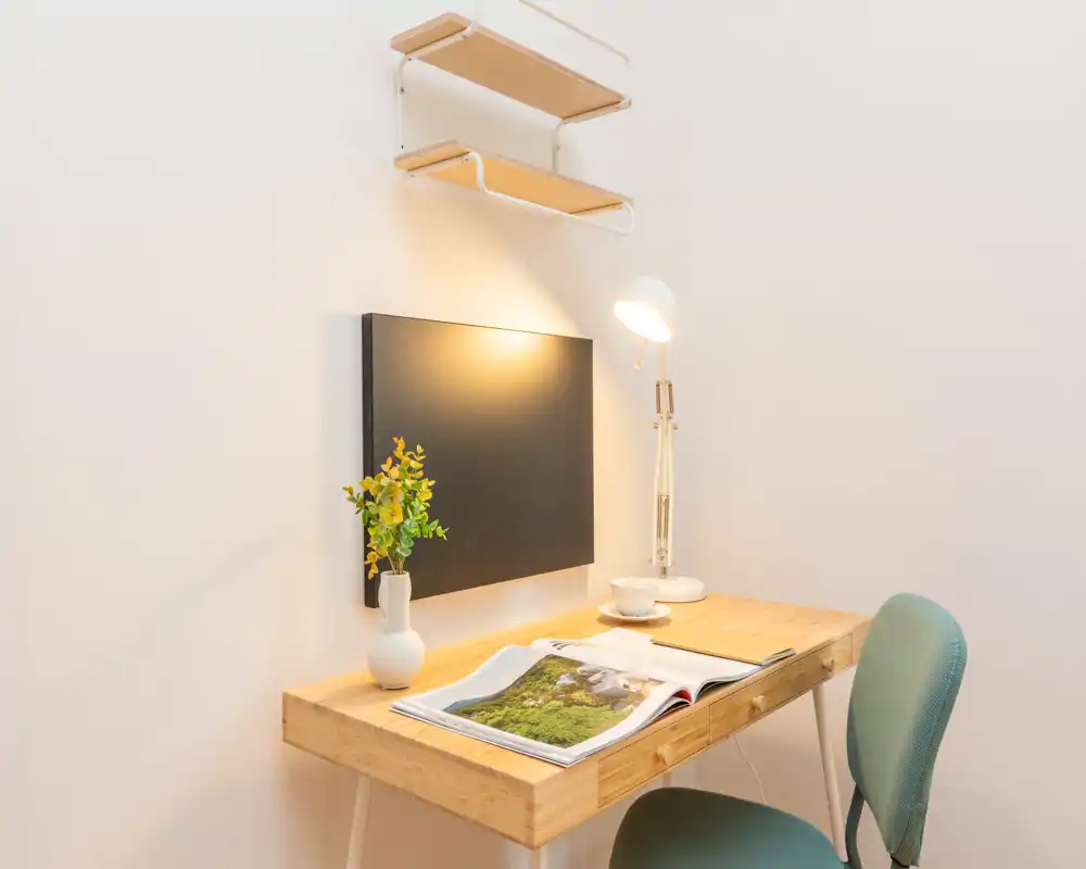 Compact, well-lit workspace corner with a wooden desk, reading lamp, small decorative plant and a comfortable chair — ideal for studying or remote work.