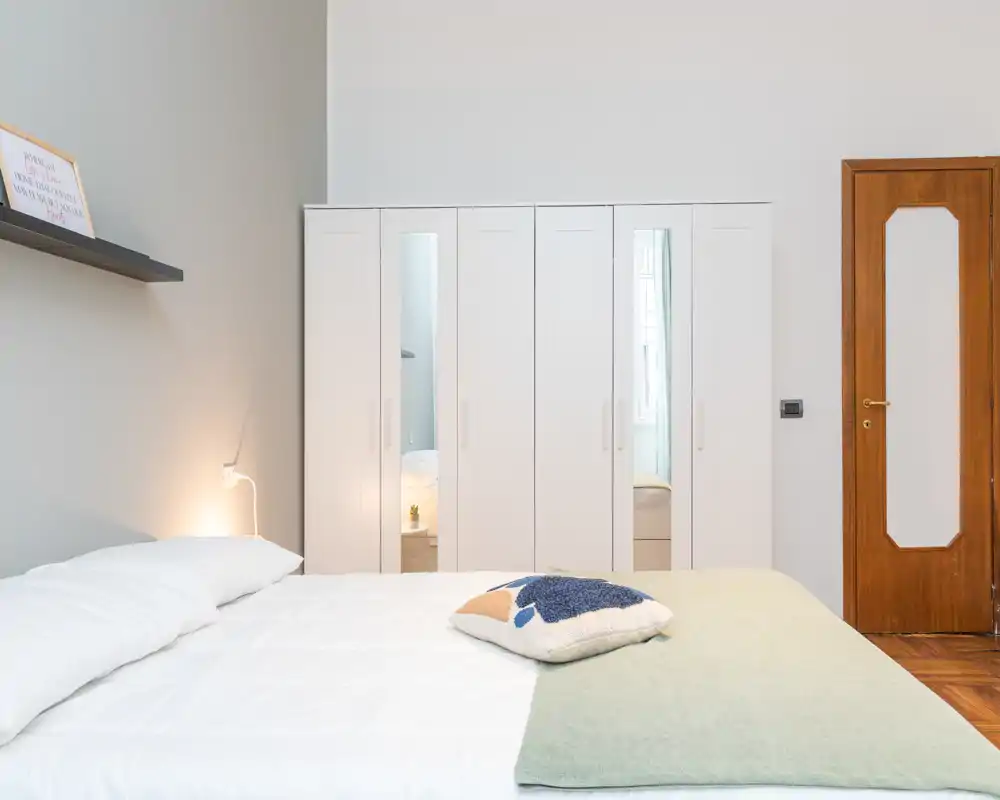Bright, modern bedroom with a neatly made double bed, soft textiles and a large white wardrobe with mirrored panels facing the bed.