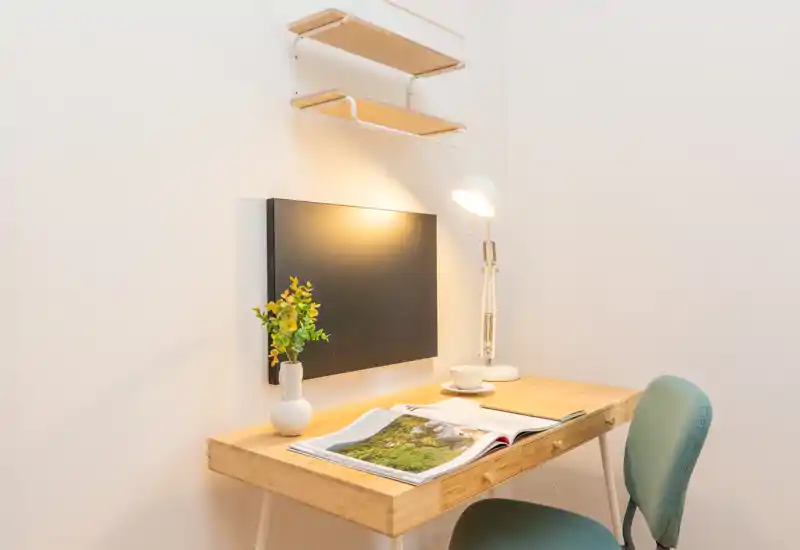 Angolo lavoro compatto e ben illuminato con scrivania in legno, lampada da lettura, piccola pianta decorativa e comoda sedia — perfetto per studiare o lavorare da remoto.
