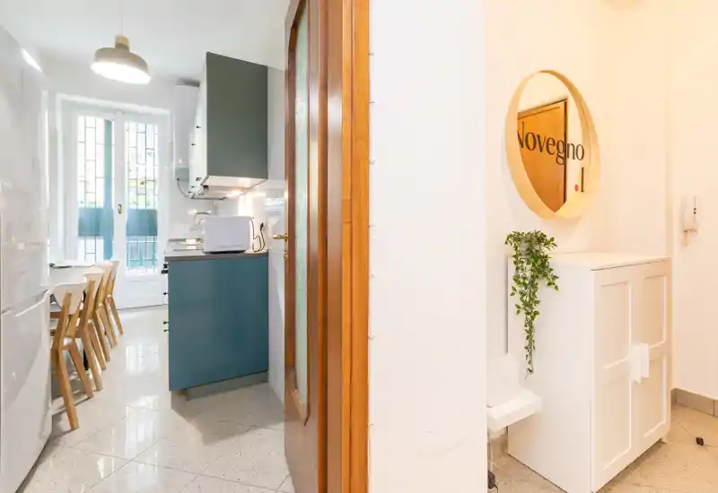 Cucina compatta e moderna con mobili verde petrolio, piccolo tavolo da pranzo e luce naturale dalla porta del balcone — ariosa, pulita e ben curata per un annuncio.