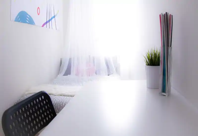 Bright, minimalist bedroom with a bed draped in a sheer canopy and soft linens. The space is styled with neutral tones and small decorative touches for a cozy feel.