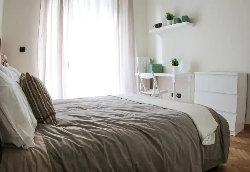 Bright, cozy bedroom with a large bed in the foreground, soft linens and a small desk by the window — ideal for restful stays.