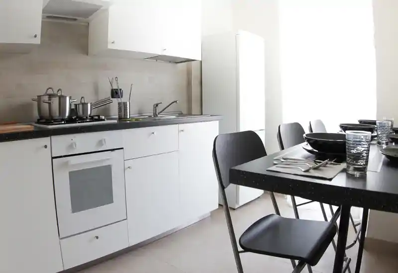 Bright modern kitchen with white cabinetry, built-in oven, sink and a small dining table set for four — ideal for compact city apartments.