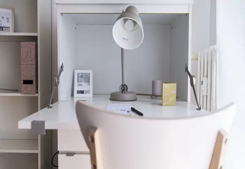 Area di lavoro luminosa e ordinata con scrivania bianca, lampada e sedia — ideale per studiare o lavorare in smart working.