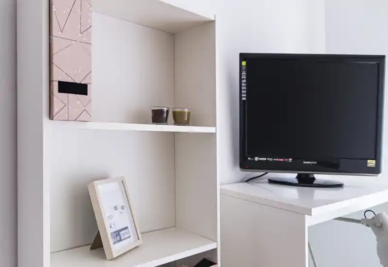 Angolo soggiorno ordinato con TV su un mobile bianco e scaffalatura minimal con oggetti decorativi.