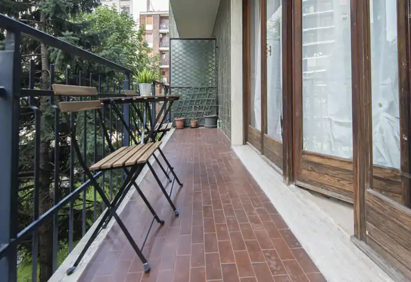 Balcone stretto e soleggiato con sedie pieghevoli in legno, ringhiera in metallo e vasi: perfetto per un caffè mattutino o per rilassarsi all'aperto.