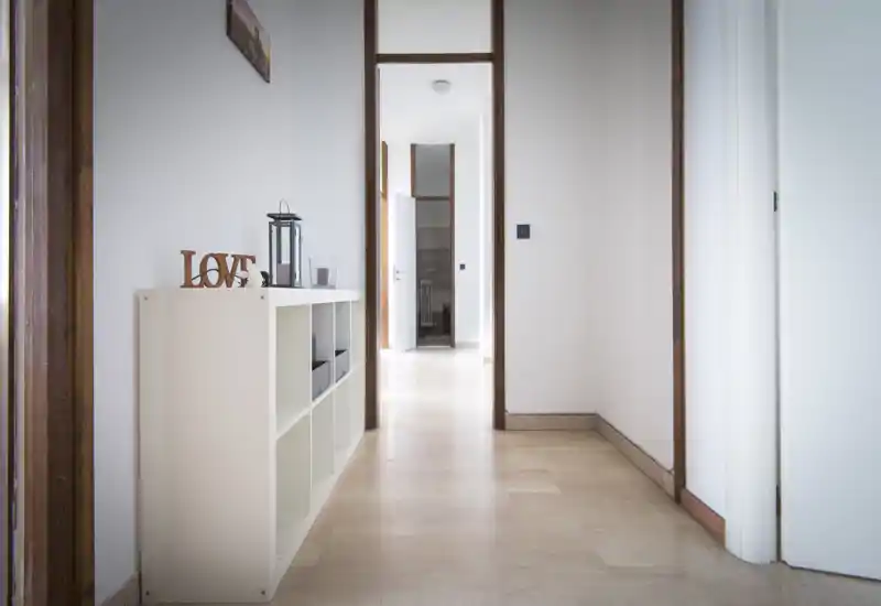 Ingresso/corridoio luminoso e minimale con pavimento chiaro, un piccolo mobile a cubi e pareti bianche pulite; si vede il proseguo verso le stanze adiacenti.