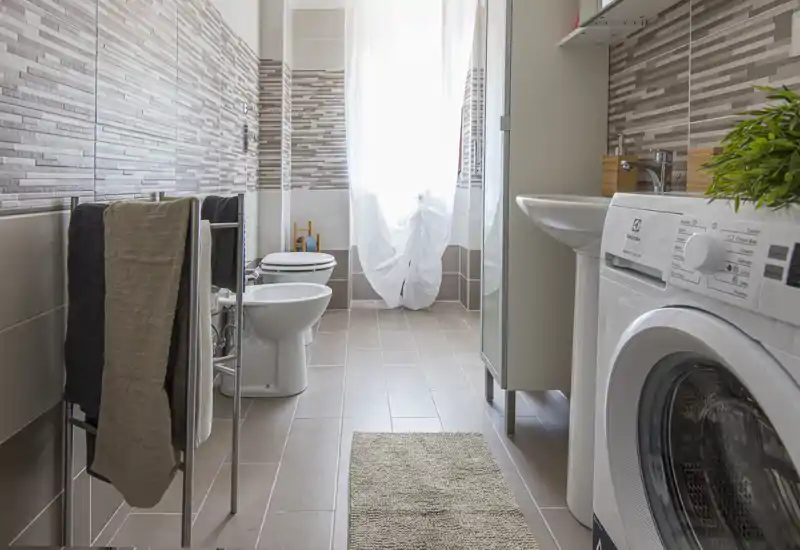 Bagno moderno e luminoso con pareti piastrellate, bidet e wc, lavabo e lavatrice — ben illuminato e ordinato.