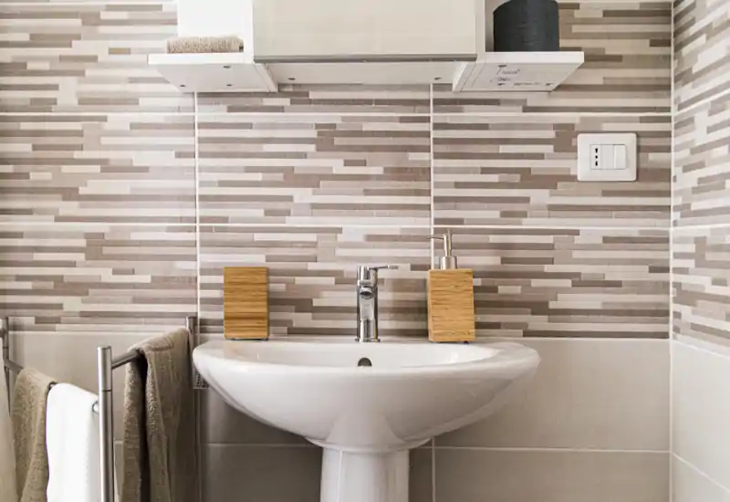Lavabo da bagno moderno e pulito con colonna, rubinetto cromato e accessori coordinati su piastrelle a motivo.