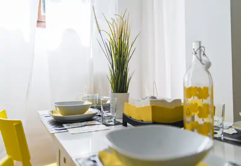 Zona pranzo luminosa e curata con tavolo apparecchiato, ciotole, bicchieri e una pianta decorativa: perfetta per pasti accoglienti.