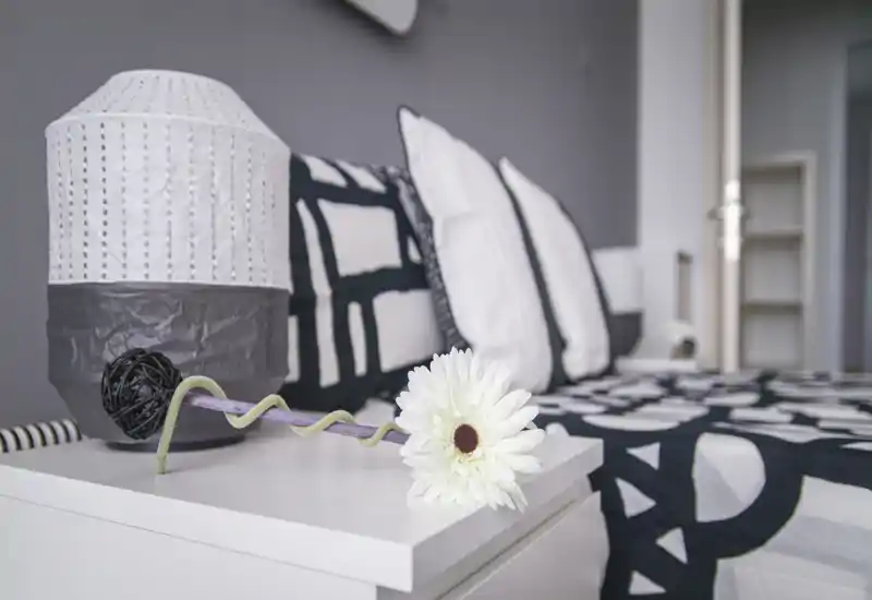 Dormitorio luminoso y con estilo centrado en la mesita de noche y la cama con cojines decorativos y lámpara, que transmite una atmósfera moderna y tranquila.