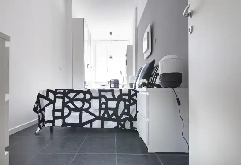 Dormitorio luminoso y minimalista con colcha estampada en blanco y negro, mesita con espacio de almacenamiento y luz natural procedente de una gran ventana — estilo moderno y limpio para anuncios.