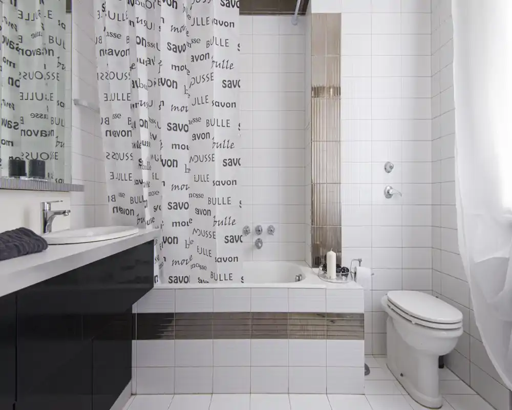 Baño moderno y limpio con bañera/ducha, azulejos blancos, inodoro y mueble con lavabo; decoración neutra y luz natural brillante.