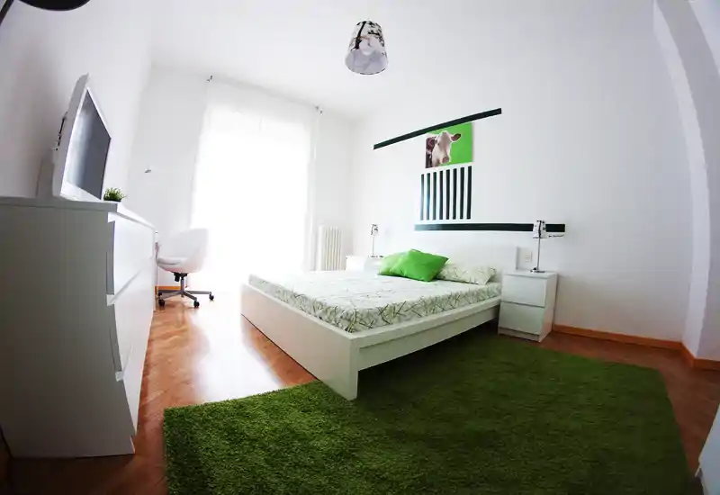 Bright, modern bedroom with a white platform bed, green accents and a large window providing abundant natural light.
