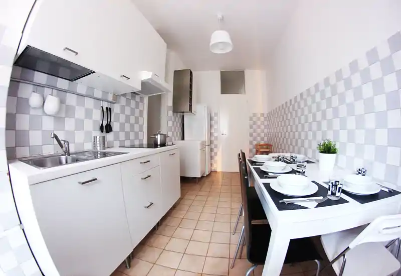 Bright, modern galley kitchen with white cabinets, checkerboard backsplash and a set dining table for four — clean, well-lit and neatly staged for guests.