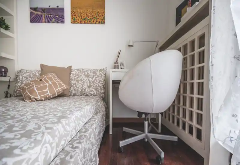 Coin chambre lumineux et chaleureux avec literie à motifs, coussins et un petit bureau avec chaise pivotante près de la fenêtre.