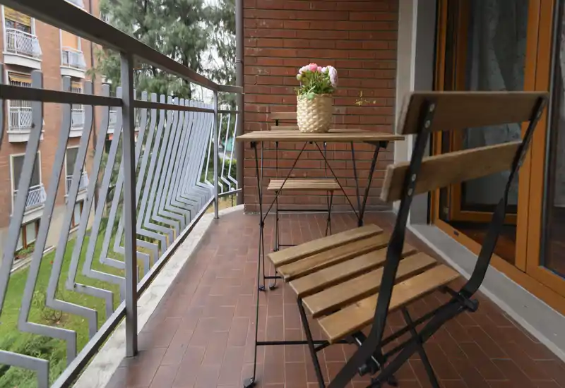 Balcone accogliente con piccolo tavolo bistro in legno e due sedie pieghevoli, una pianta in vaso sul tavolo e vista sul cortile—perfetto per il caffè mattutino.