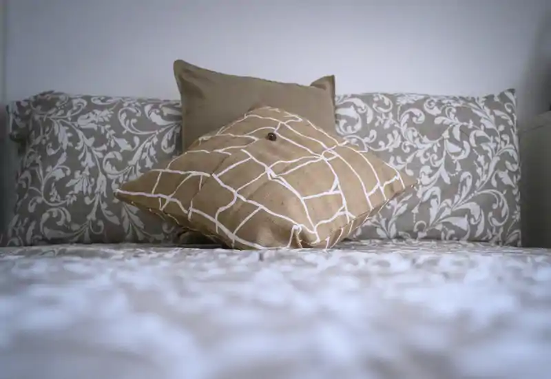 Chambre chaleureuse en gros plan avec une tête de lit à motifs et des coussins décoratifs sur un lit bien fait, lumière naturelle douce et tons neutres.