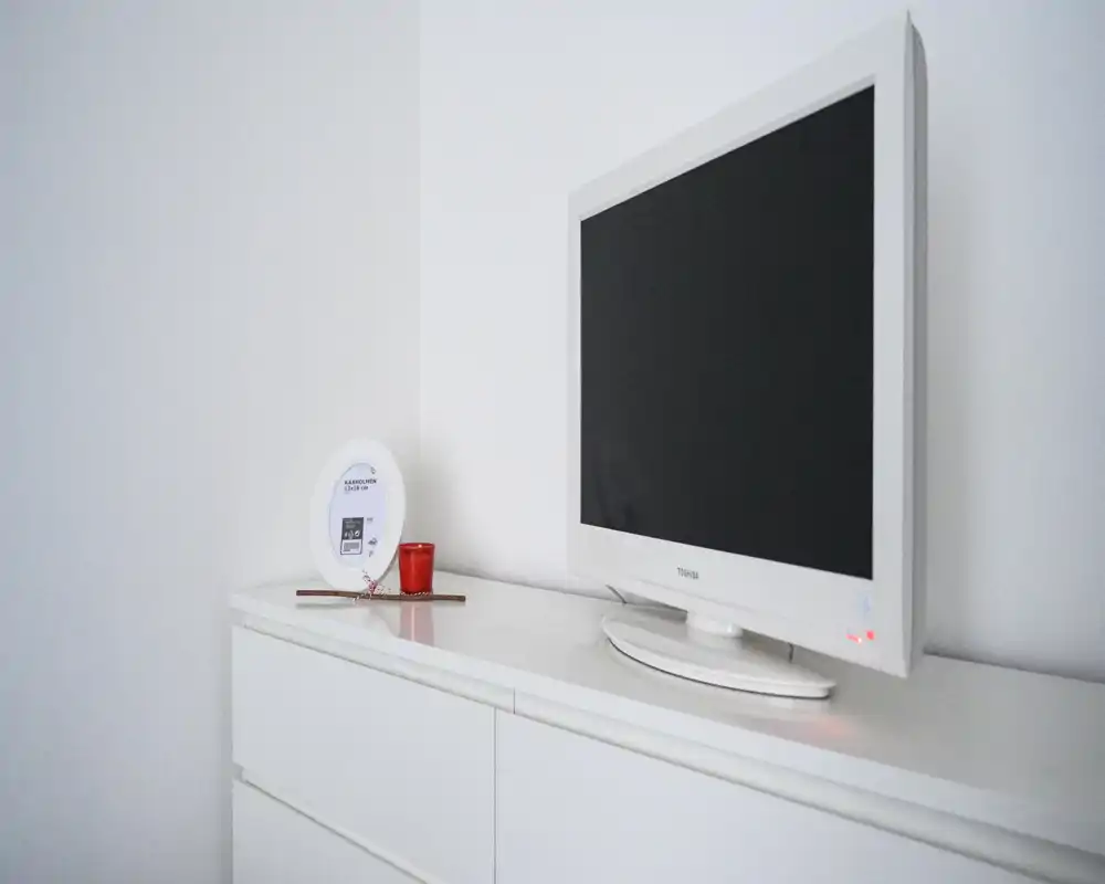 Detalle luminoso y minimalista del salón con un televisor blanco sobre una cómoda a juego, una vela decorativa y un portarretratos que aportan un aspecto limpio de estilo escandinavo.