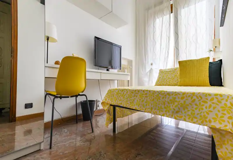 Bright, modern bedroom with a yellow floral bedspread, matching cushions and a small desk with a TV — ideal for a cheerful single or double stay.