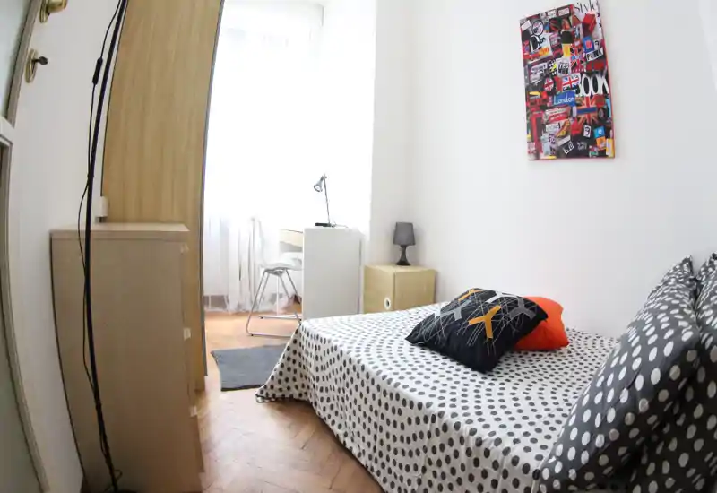 Dormitorio compacto y luminoso con funda de lunares, cojines decorativos y un pequeño escritorio junto a la ventana. La luz natural y el mobiliario moderno ofrecen un ambiente acogedor y funcional, ideal para estancias cortas.