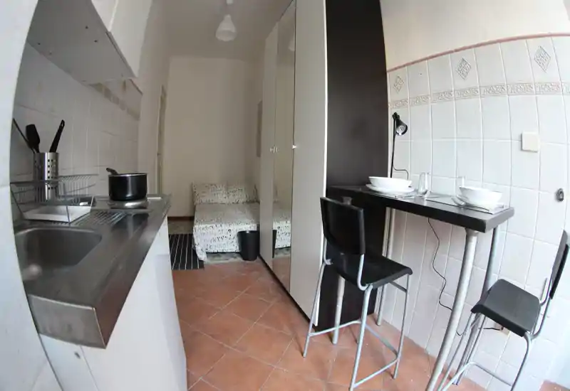 Monolocale compatto con angolo cottura con lavello e piano cottura, un armadio alto e una piccola zona letto/seduta; ideale per una persona o soggiorni brevi.