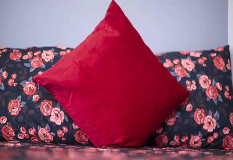 Close-up of a bedroom bed area with floral bedding and a prominent red throw cushion, creating a warm, decorative accent.