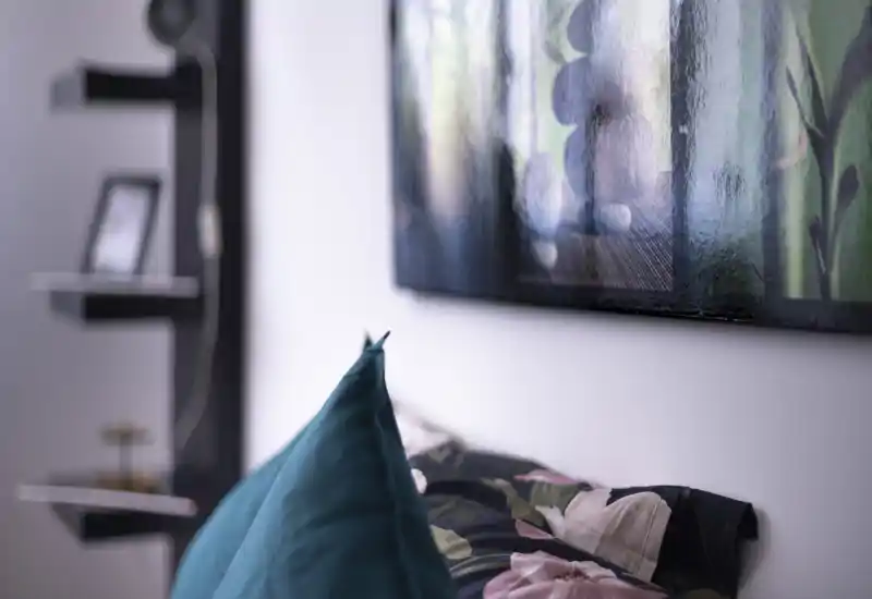 Close-up bedroom detail showing decorative pillows and part of the bed with a framed artwork above; soft, styled composition ideal for a cozy listing photo.