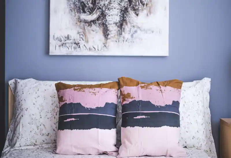 Bright, styled bedroom close-up featuring patterned pillows and a floral sheet against a soft blue wall — ideal for cozy listing photos.