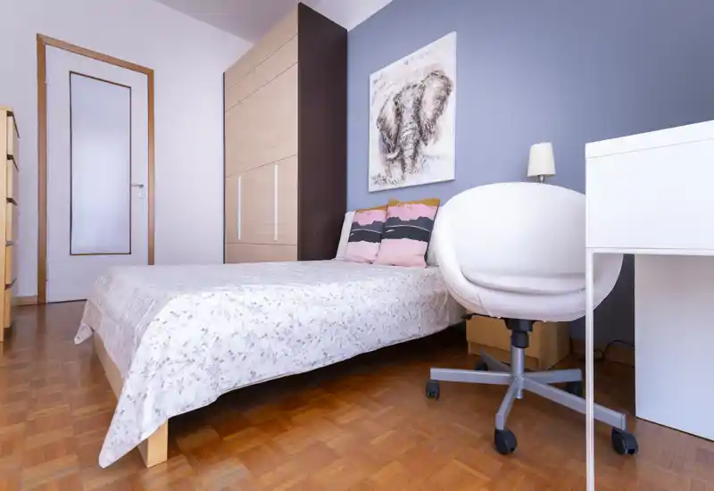 Bright, tidy bedroom with a double bed, wardrobe and a desk area. Soft pillows and neutral decor create a calm, inviting atmosphere ideal for rental listings.