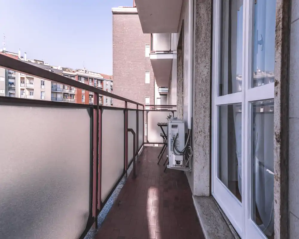 Balcón estrecho y soleado con paneles de vidrio esmerilado, suelo de terracota y una mesita pequeña — ideal para el café de la mañana con vistas a la ciudad.
