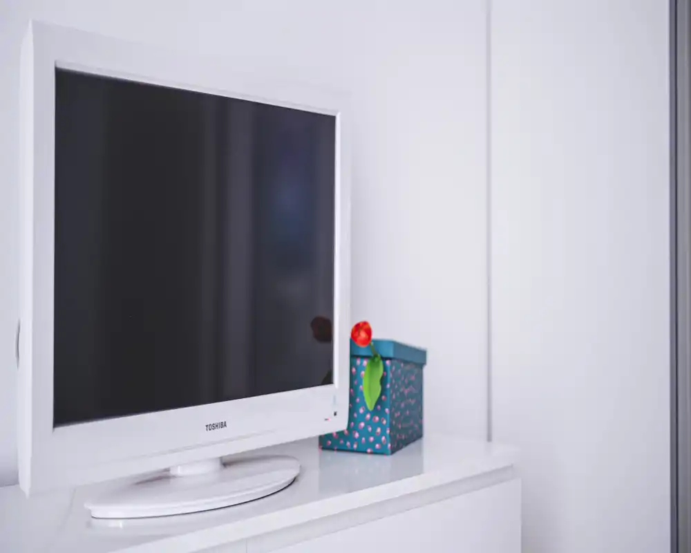Imagen de una zona de estar minimalista con un televisor blanco sobre un mueble elegante y una caja decorativa; luminoso, ordenado y moderno.