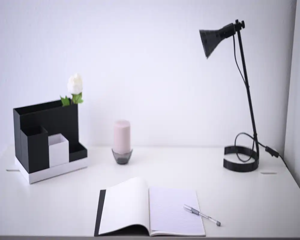 Angolo di lavoro minimal e luminoso con scrivania bianca, quaderno aperto, penna, lampada da tavolo e piccolo organizer con una candela — un tranquillo e moderno spazio per lavorare.