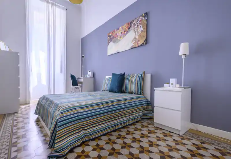 Bright, stylish bedroom with a double bed dressed in colorful striped bedding, tall window with sheer curtains, bedside tables and decorative artwork above the headboard.