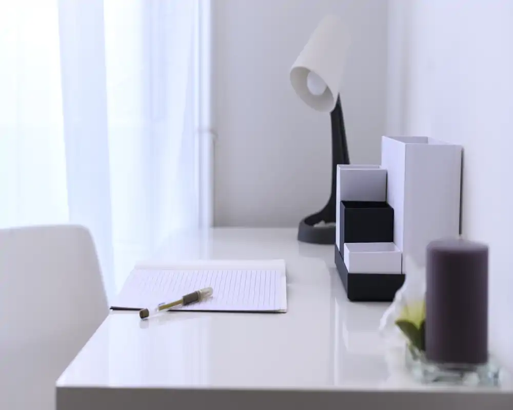 Angolo di lavoro luminoso e minimal con scrivania bianca, lampada da tavolo e candela decorativa — un angolo tranquillo ideale per leggere o lavorare leggermente.