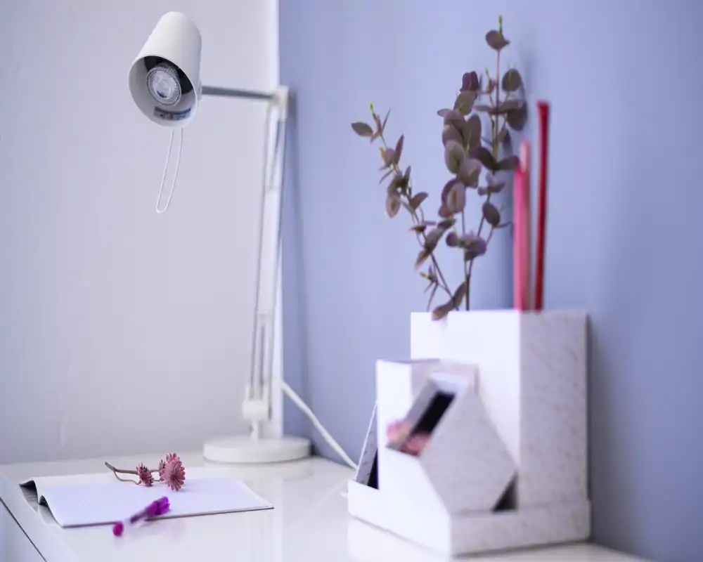 Close-up of a tidy bedside or desk area with a table lamp, notepad, decorative flowers and a small organizer — a calm, styled corner suitable for a bedroom or workspace.
