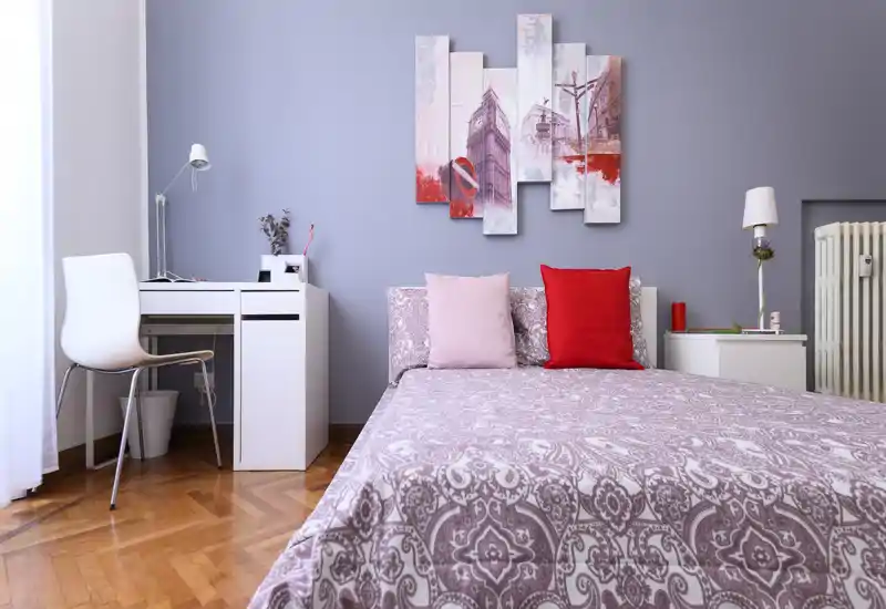 Well-styled bedroom with patterned bedding, decorative pillows and a small desk by the window; bright natural light and coordinated wall art create a fresh, welcoming space.
