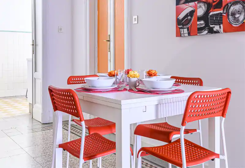 Bright, styled dining area with a white table set for four and vibrant red chairs — a cheerful, modern spot for meals.