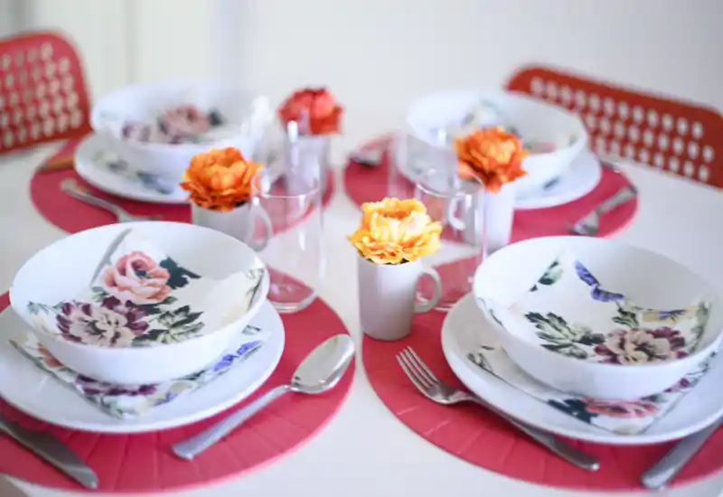 Stylish dining table set for four with bright pink placemats, floral napkins and small flower centerpieces — ideal for a cheerful meal.