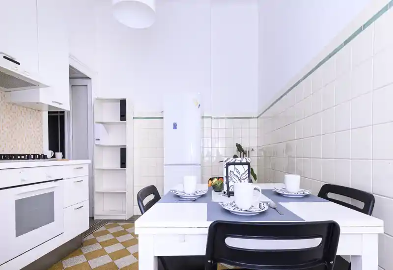 Bright, modern kitchen with a white table set for four, a freestanding fridge and white cabinetry. The tiled walls and patterned floor add character while the table styling creates a welcoming dining corner.