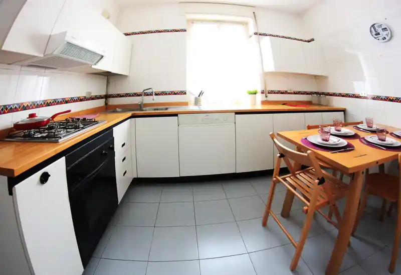 Bright, compact kitchen with wooden worktops, built-in oven and dishwasher, and a small dining table set for four — clean and well staged for rental photos.