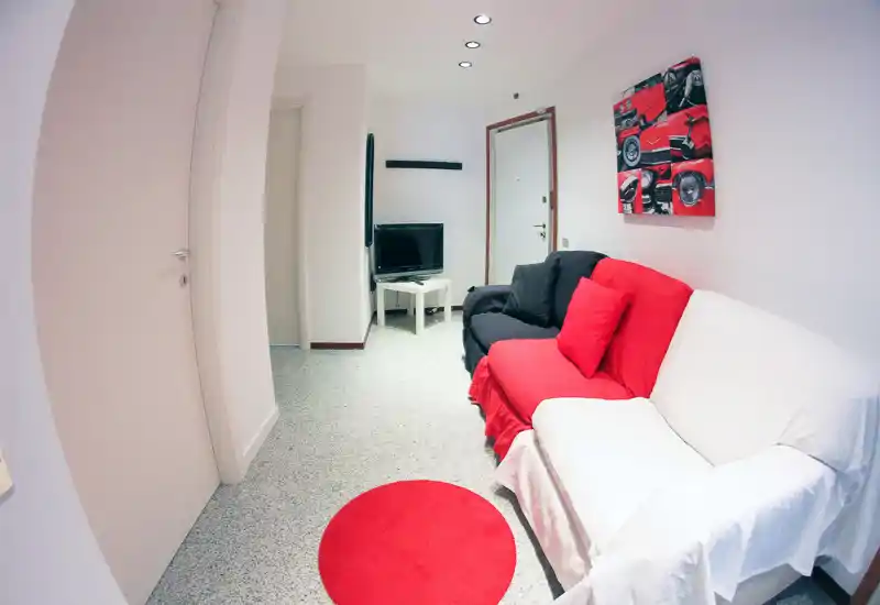 Compact living room with a red-and-white sofa arrangement, matching round rug and wall art. The space is well lit and furnished for casual seating and TV viewing.